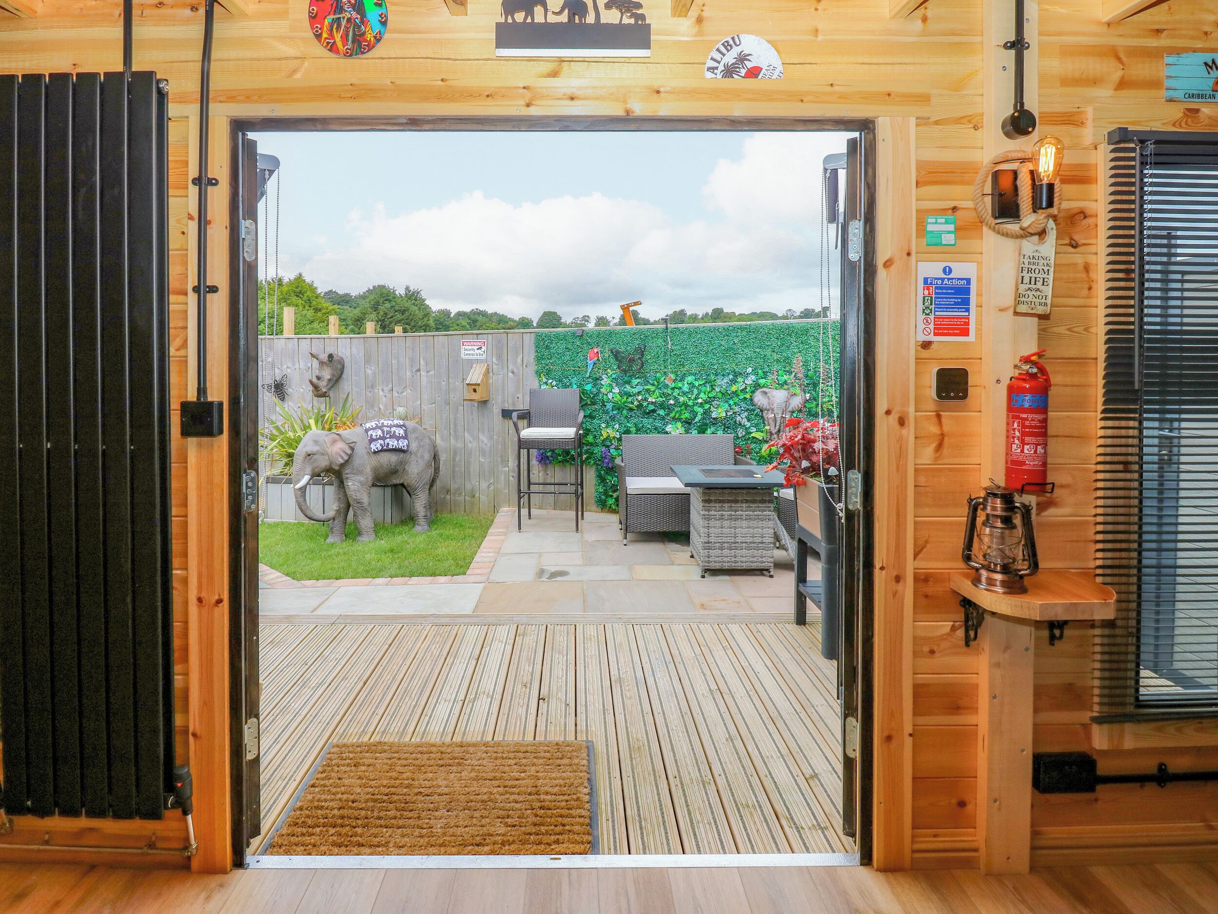 Een houten interieur met een deur naar een terras buiten, met een brandblusser, een lantaarn en een tafel met stoelen.
