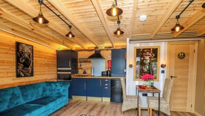 Interior acogedor de una cabaña con un sofá azul, zona de cocina y comedor con sillas de mimbre.