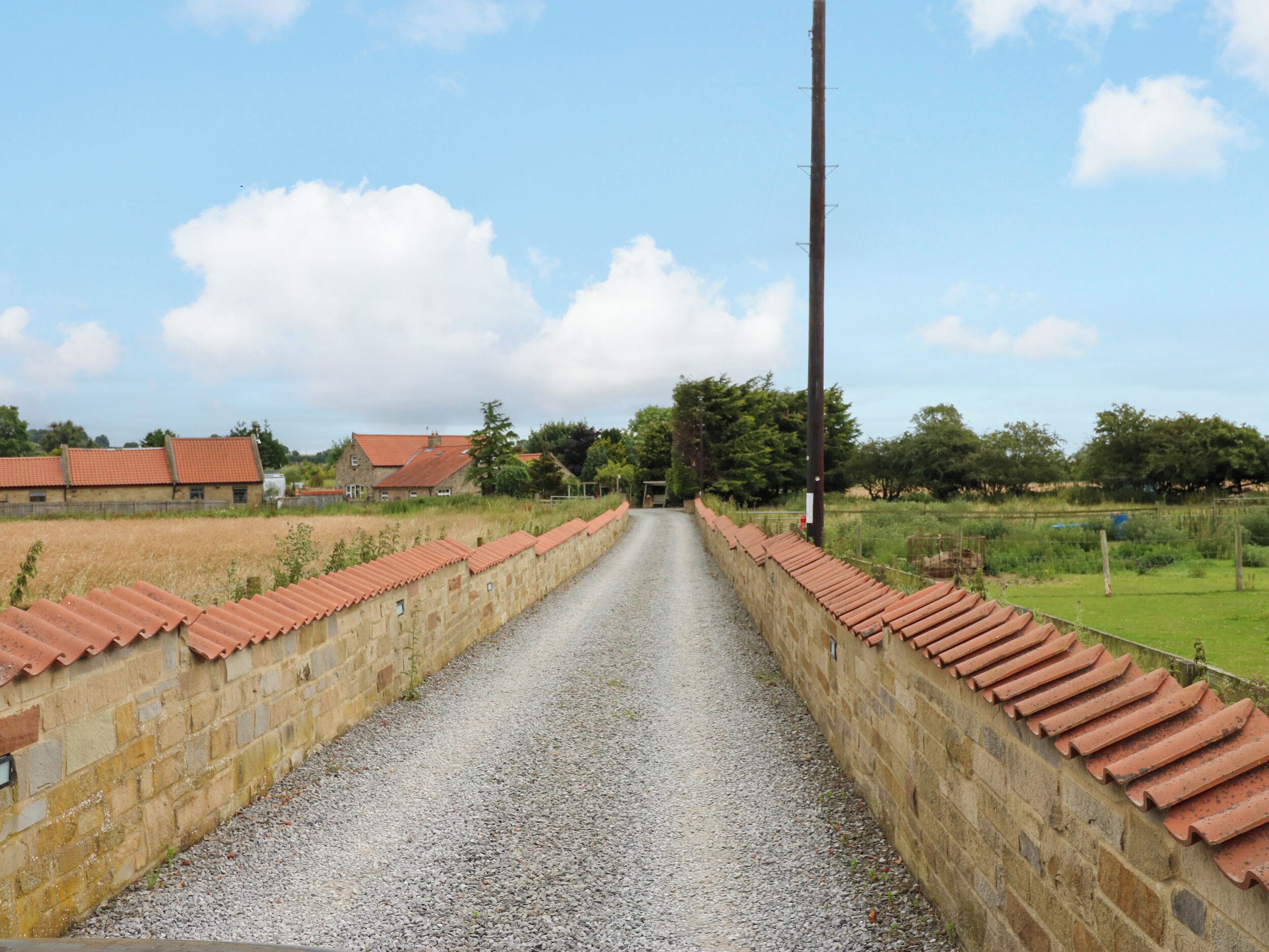 A gravel path leading to a stone wall with a red-tiled roof.