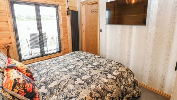 Un dormitorio con cama, ventana con persianas, puerta y estante fijado a la pared.