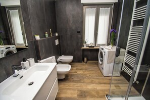 Ett modernt badrum med en stor, vit tvättställ, en toalett, en tvättmaskin och en duschkabin med glasväggar.