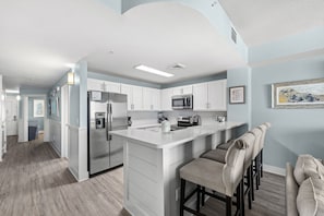Una cocina moderna con armarios blancos, electrodomésticos de acero inoxidable y una barra con taburetes acolchados.