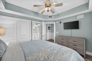 A bedroom with a bed, a dresser, a ceiling fan, a television, and a door leading to another room. - stunning Gulf views, resort-style amenities, and an unbeatable location (Panama City Beach)