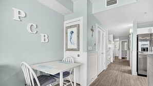 Una cocina moderna con armarios blancos, un refrigerador de acero inoxidable y un comedor con mesa y sillas blancas.