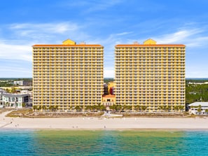 Um hotel à beira-mar com dois edifícios amarelos de destaque, uma praia de areia e um céu azul claro.