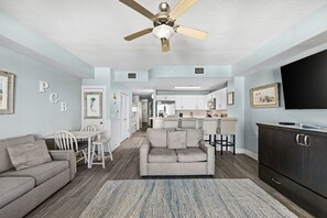 A modern living room with a grey sofa, a dining area with a white table, and a kitchen in the background. - stunning Gulf views, resort-style amenities, and an unbeatable location (Panama City Beach)