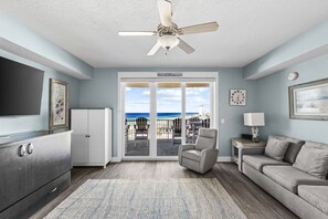 A living room with a television, a sofa, a chair, a ceiling fan, and a view of the beach through the glass doors. - stunning Gulf views, resort-style amenities, and an unbeatable location (Panama City Beach)