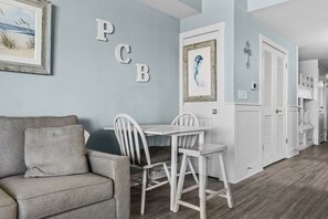 A room with a grey sofa, a white dining table with chairs, and a wall with letters 'PCB' and a framed artwork. - stunning Gulf views, resort-style amenities, and an unbeatable location (Panama City Beach)