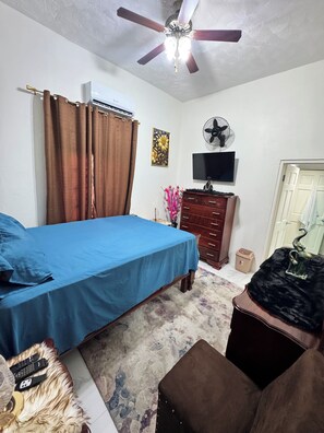 A bedroom with a bed, a dresser, a television, and a ceiling fan. - Content Luxury Stay – Where Comfort Meets Luxury (Spanish Town)