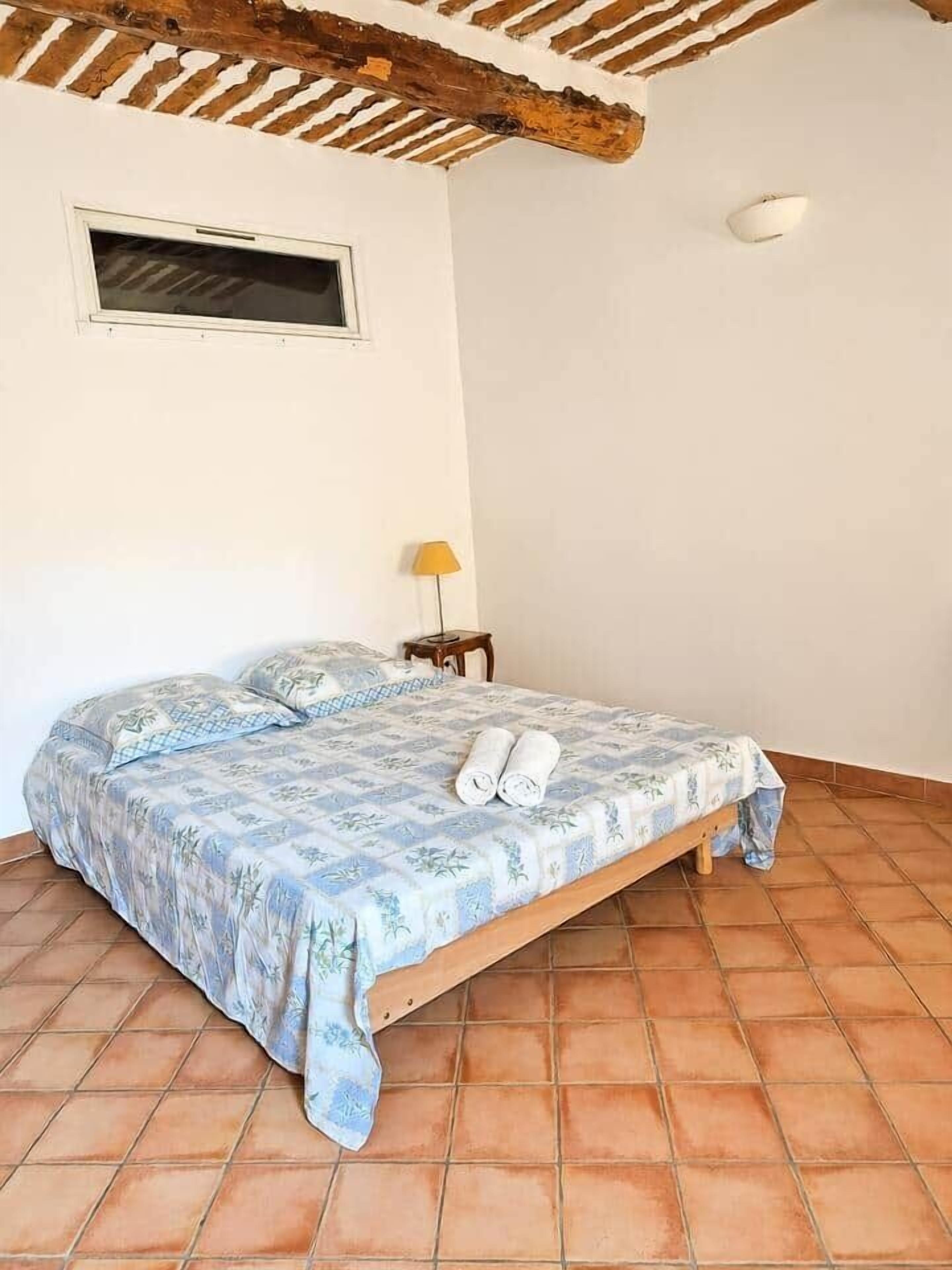 Un llit individual amb un estovat estampat, una petita taula de nit amb una làmpada i una finestra.