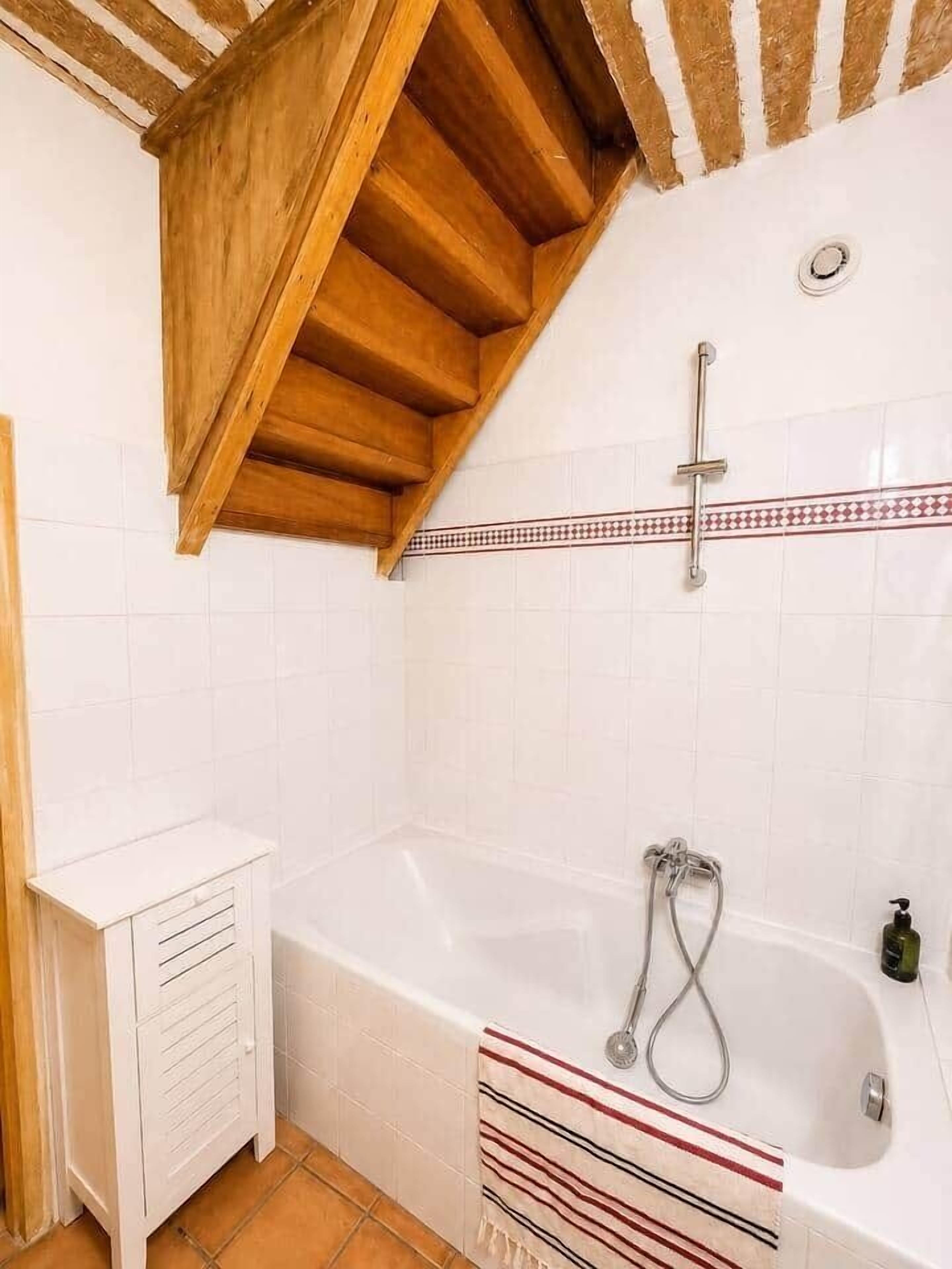 A bathroom with a wooden staircase, a bathtub, and a shower area.