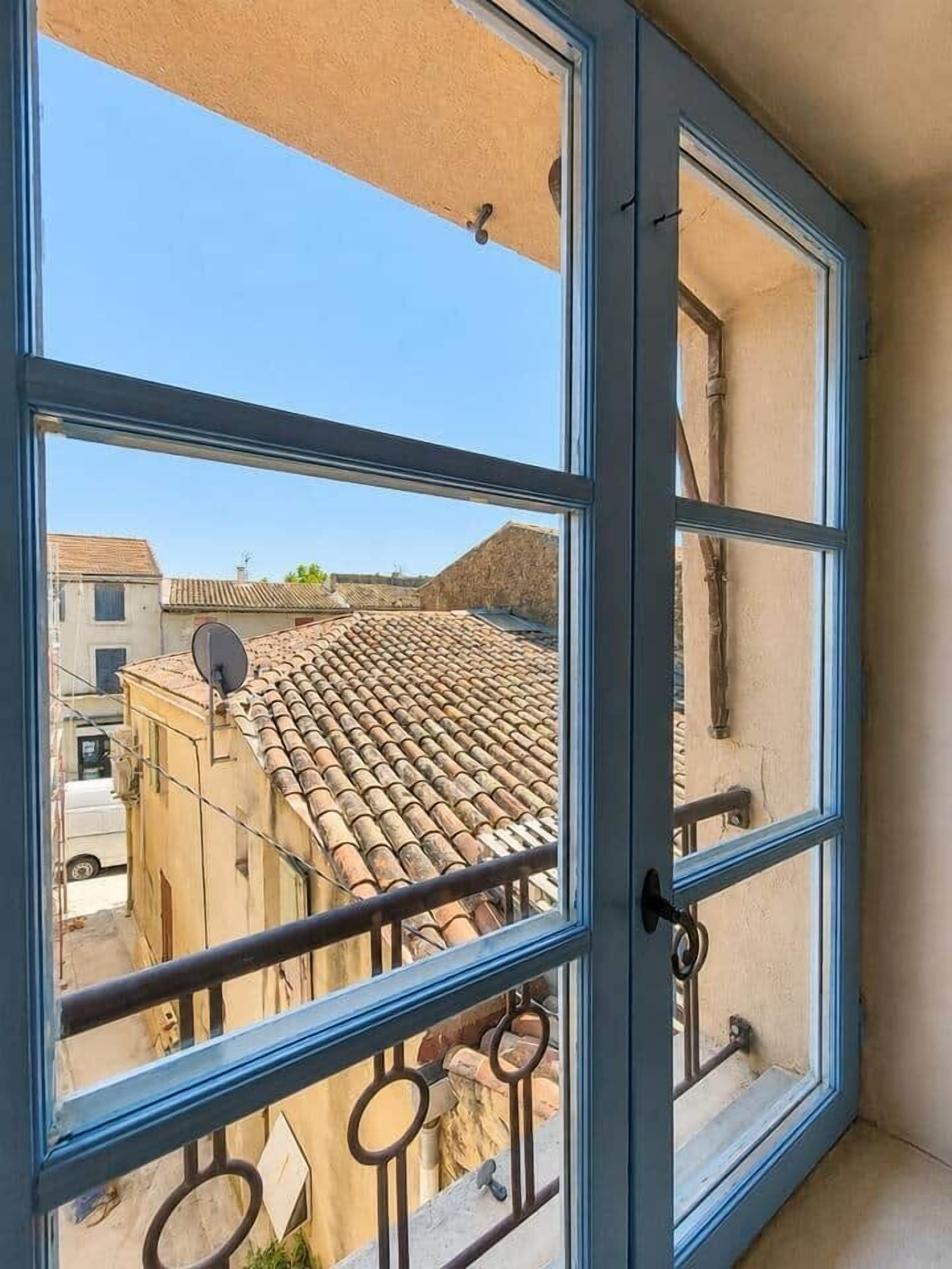 A window with a view of a building's tiled roof and a satellite dish.