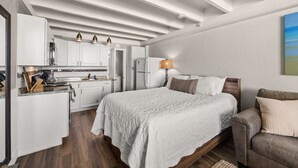 Ein gemütliches Schlafzimmer mit Bett, Nachttisch und Beistelltisch. Es gibt eine Küchenzeile mit Kühlschrank, Herd und Schränken.
