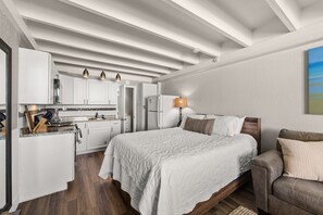 A compact bedroom with a bed, bedside table, and a nightstand. There is a kitchenette with a refrigerator, stove, and cabinets. - Beachfront Studio at Fontainebleau | Private Beach Access (Panama City Beach)