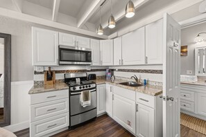 A kitchen with white cabinets, a stainless steel stove, a microwave, and a granite countertop. - Beachfront Studio at Fontainebleau | Private Beach Access (Panama City Beach)