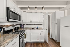 Une cuisine avec des armoires blanches, un four à micro-ondes, une cuisinière et un réfrigérateur. Trois lampes suspendues sont fixées au plafond.
