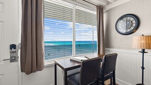 Ein Zimmer mit Tisch und Stühlen, einem Fenster mit Jalousien, einer Wanduhr und einer Lampe.