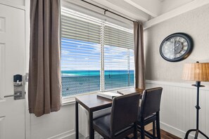 A room with a table and chairs, a window with blinds, a clock on the wall, and a lamp. - Beachfront Studio at Fontainebleau | Private Beach Access (Panama City Beach)