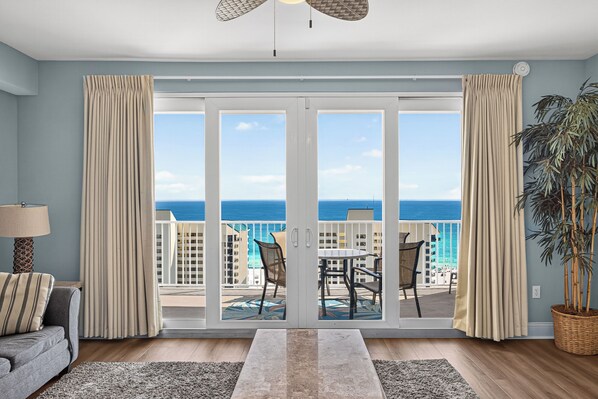 A room with a large sliding glass door leading to a balcony with a view of the ocean and buildings. There is a sofa, a table with chairs, and a potted plant. - Coastal Comfort with Gulf Views at Laketown Wharf 1416 (Panama City Beach)