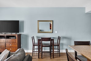 A dining area with a table and chairs, a flat-screen TV on a wooden cabinet, and a mirror on the wall. - Coastal Comfort with Gulf Views at Laketown Wharf 1416 (Panama City Beach)