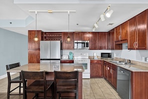 A kitchen with wooden cabinets, stainless steel appliances, a granite countertop, and pendant lighting. - Coastal Comfort with Gulf Views at Laketown Wharf 1416 (Panama City Beach)