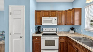 Una cocina con armarios de madera, microondas, estufa, cafetera y lavaplatos.