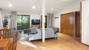 Ein modernes Wohnzimmer mit grauem Sofa, Holzstühlen, einem Flachbildfernseher und einem großen Holzschrank.