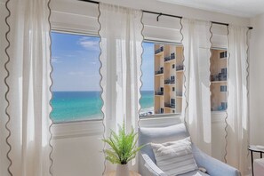 Ein Zimmer mit Meerblick, ein Sessel, eine Pflanze und ein Fenster mit Vorhängen.