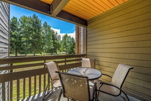 A covered outdoor seating area with a table and chairs, a wooden railing, and a view of trees and sky. - Mountain Days and Hot Tub Nights | Private Balcony (Steamboat Springs)