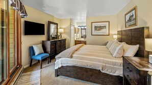 A bedroom with a bed, dresser, chair, and a television. - 2BR Mountain Condo | Walk to Resort, Hot Tubs, Pool (Steamboat Springs)