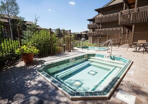 Ett poolområde med två bubbelpooler, ett trästaket och en byggnad med balkonger.