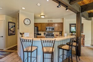 Cocina con armarios de madera, un refrigerador de acero inoxidable, microondas y barra con tres taburetes.
