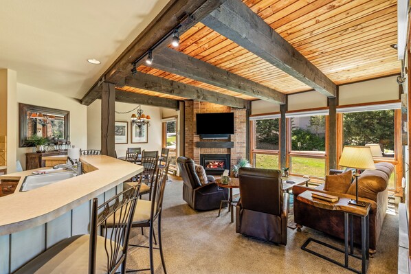 A spacious living area with a fireplace, a bar, and a large window offering a view of the outdoors. - Mountain Days and Hot Tub Nights | Private Balcony (Steamboat Springs)