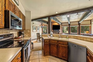 A modern kitchen with wooden cabinets, a built-in oven, a dishwasher, and a large window providing natural light. - Mountain Days and Hot Tub Nights | Private Balcony (Steamboat Springs)