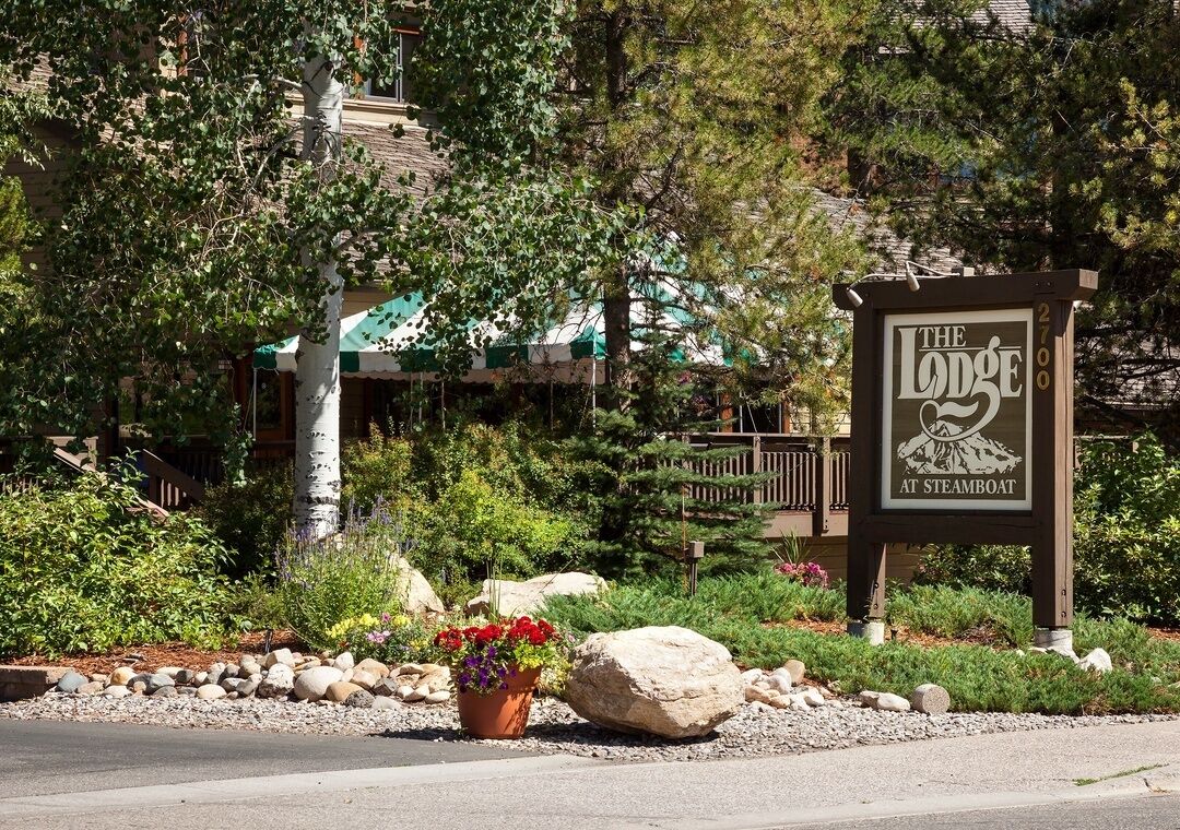 A sign for 'The Lodge at Steamboat' with a mountain and tree design, surrounded by a landscaped garden with rocks and a potted plant.
