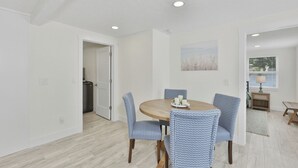 Un comedor con una mesa redonda, sillas estampadas en azul, un techo con iluminación empotrada y una puerta que da a una cocina.