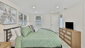 Un dormitorio con cama, televisor, cómoda y puerta que da a otra habitación.