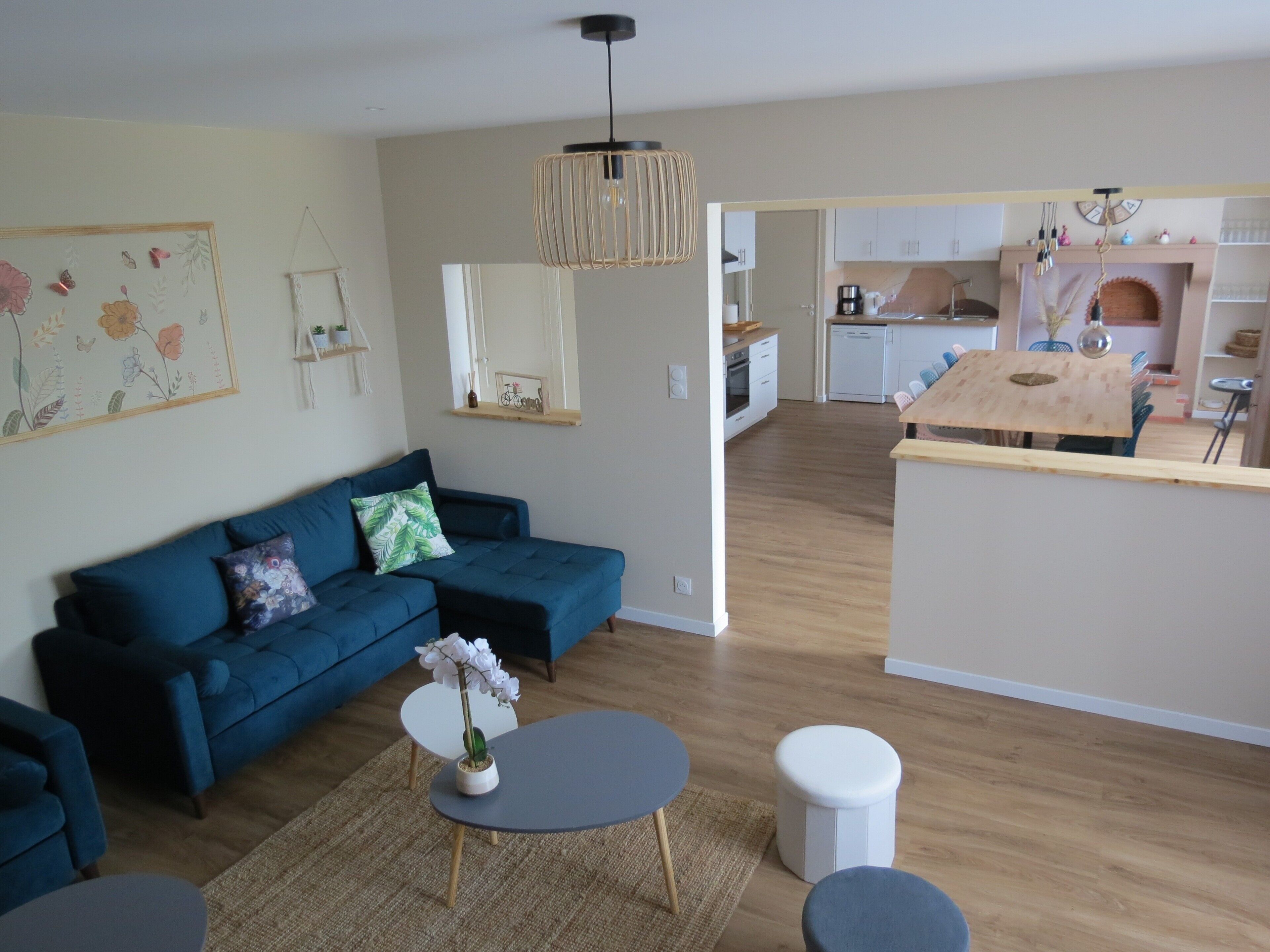 A modern living room with a blue sofa, a round coffee table, and a small white table. A kitchen is visible in the background with white cabinets and a wooden countertop.