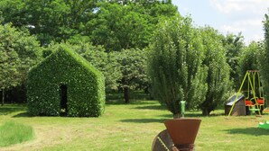 Un jardín con setos podados, una carretilla y una pequeña construcción de madera.