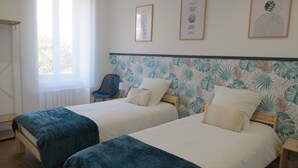 Una habitación con dos camas, una silla, un ventanal y decoración en la pared.