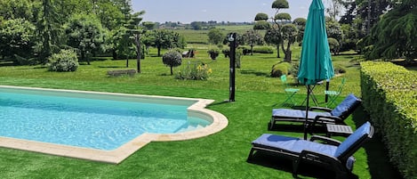 A swimming pool with a surrounding lawn, lounge chairs, and a green umbrella.