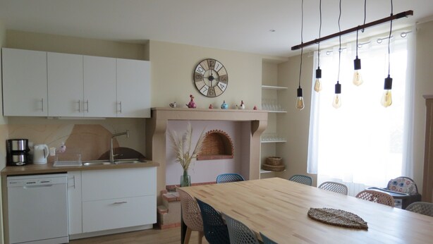 Una cocina moderna con armarios blancos, una mesa de comedor de madera y una chimenea de ladrillo integrada.