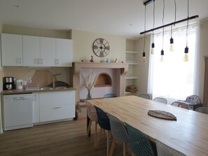 A modern kitchen with white cabinets, a wooden dining table, and a built-in brick fireplace. - Gîtes De L'Hommé - La Petite Bohème with Shared Pool, Private Terrace, and Wi-Fi (Coust)