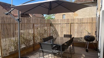 Um pátio com mesa e cadeiras, churrasqueira e um grande guarda-sol.