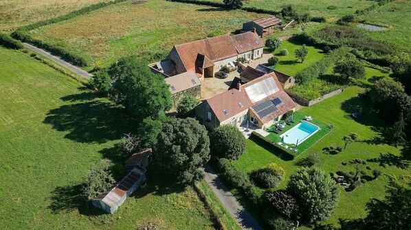An aerial view of a property with a large house, a swimming pool, and surrounding green fields.