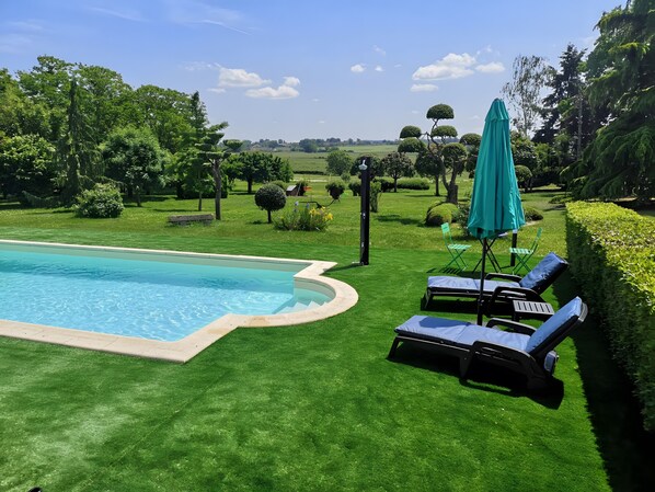 A swimming pool with a surrounding lawn, lounge chairs, and a green umbrella.