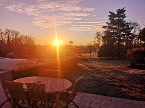 A sunset view with a table and chairs in the foreground, a tree to the right, and a clear sky.