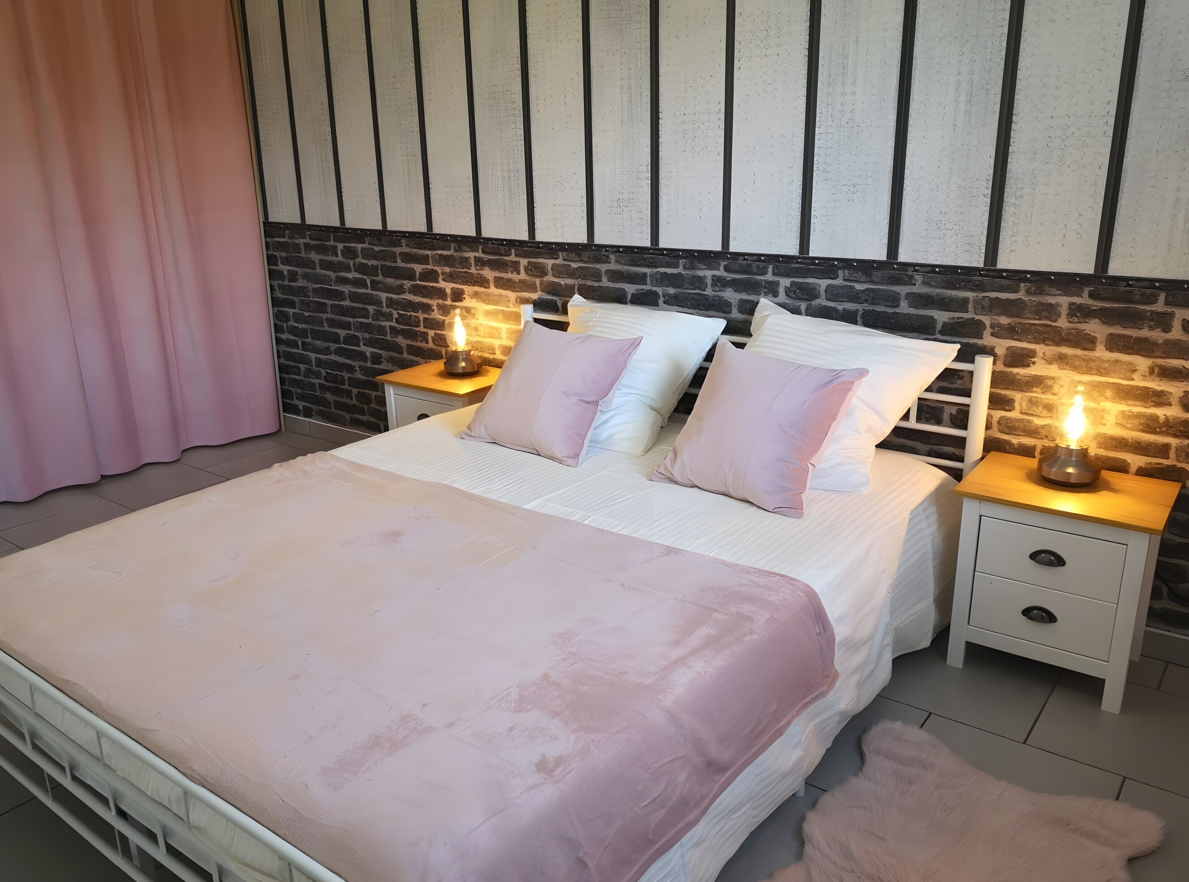 Une chambre avec un mur en briques, un lit blanc avec une literie rose, deux tables de chevet avec des lampes et une table de nuit en bois.