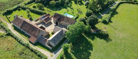 An aerial view of a property with multiple buildings, a swimming pool, and surrounding green fields.