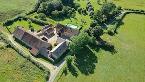 An aerial view of a property with multiple buildings, a swimming pool, and surrounding green fields.